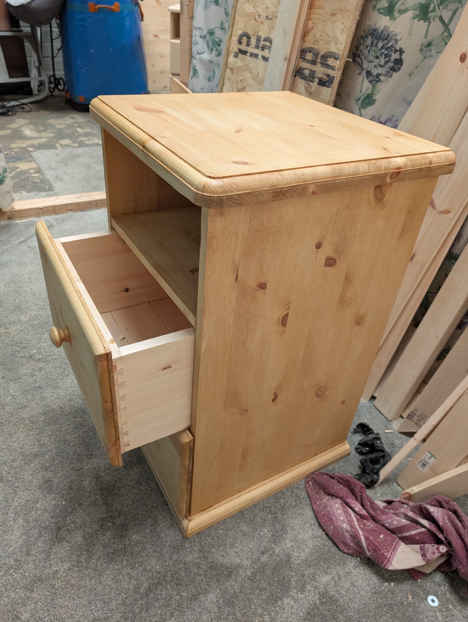 Close-up of a drawer pulled from a bedside cabinet in the workshop, showing the hand-cut dovetail joints at the corners of the drawer box.